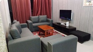 A living room with grey sofas, a wooden coffee table, a TV on the wall, and a red curtain.