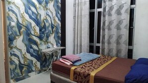 A bedroom with a bed, a window with curtains, and a wall with a marble-like pattern.