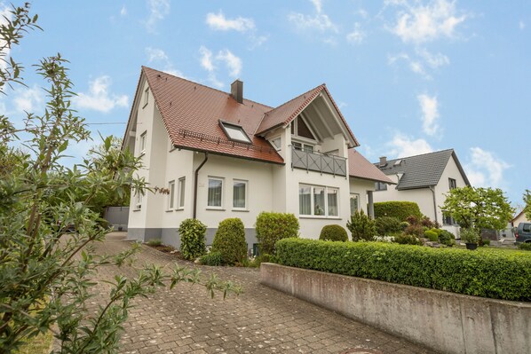 Une maison à deux étages, avec un toit en tuiles, un balcon et une allée pavée.