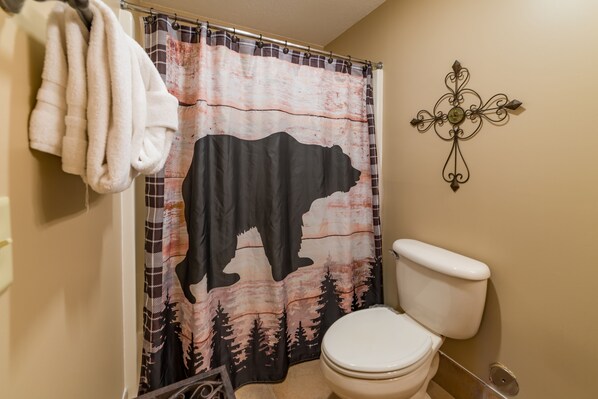 A bathroom with a bear-themed shower curtain, a toilet, and a decorative wall piece.