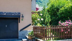 Un bâtiment avec une porte de garage sombre, un mur de pierre et une clôture en bois ornée de fleurs roses.