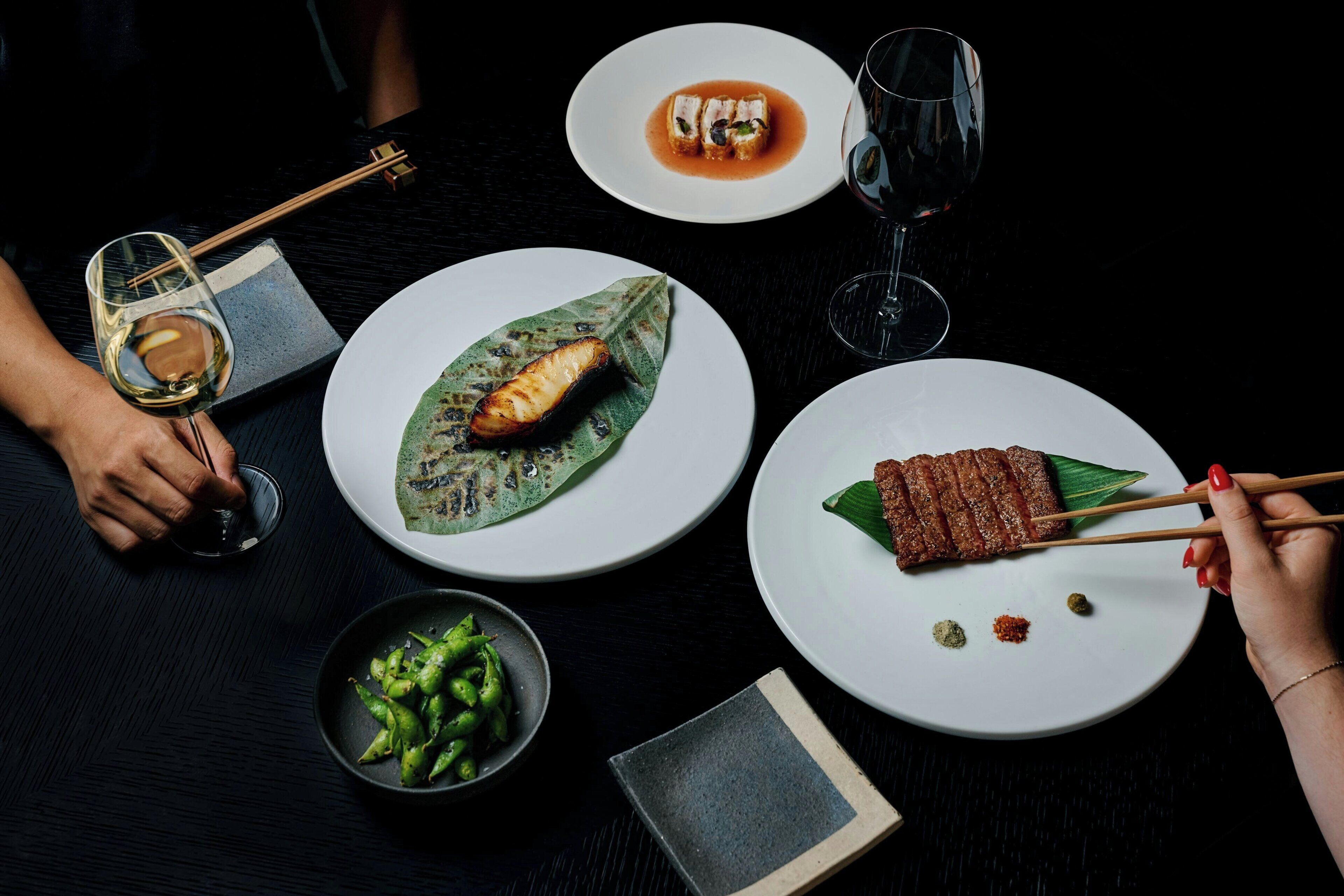 A table with various dishes, chopsticks, and glasses of wine.