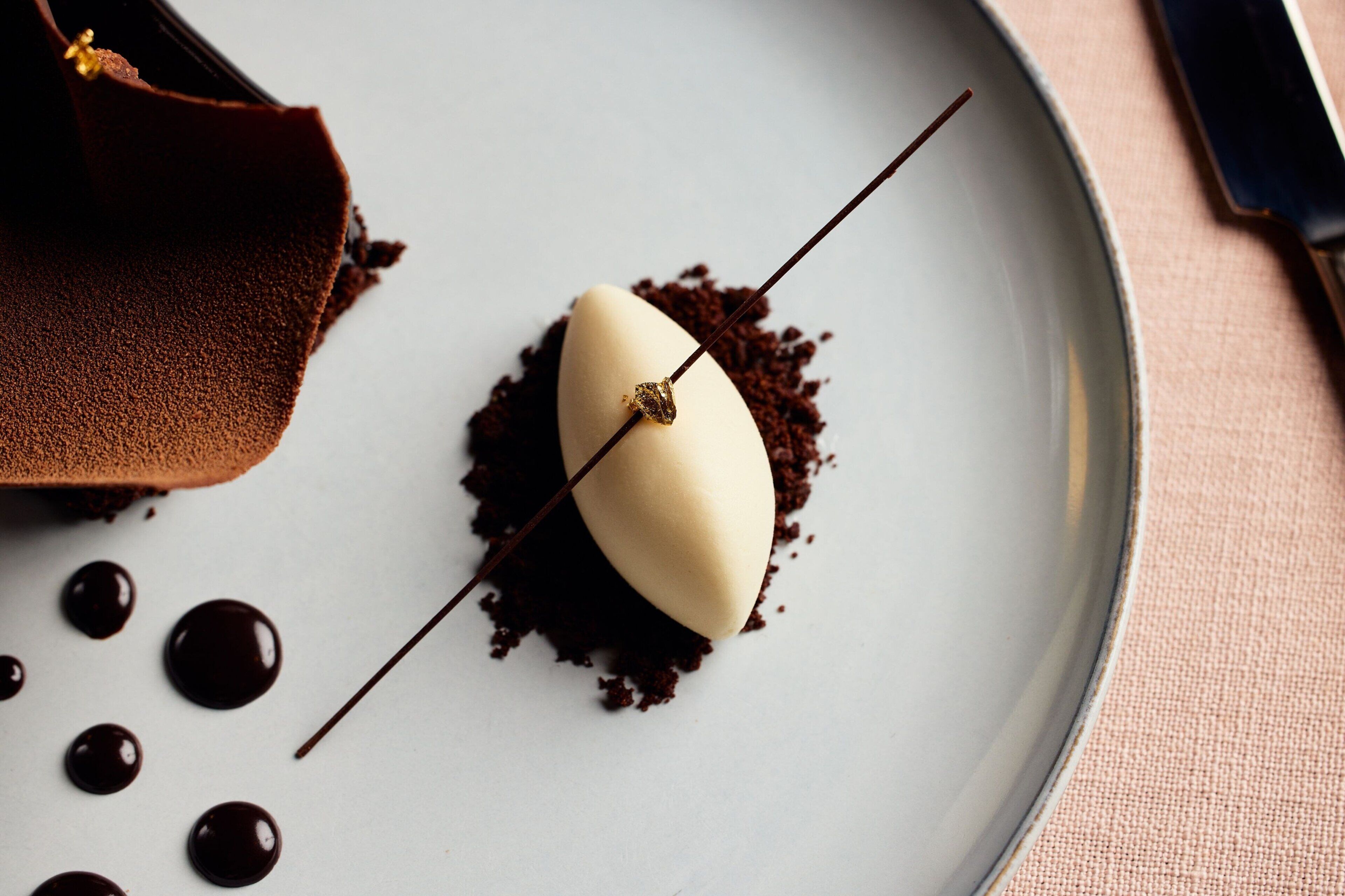 A dessert on a plate with chocolate shavings and chocolate drops.