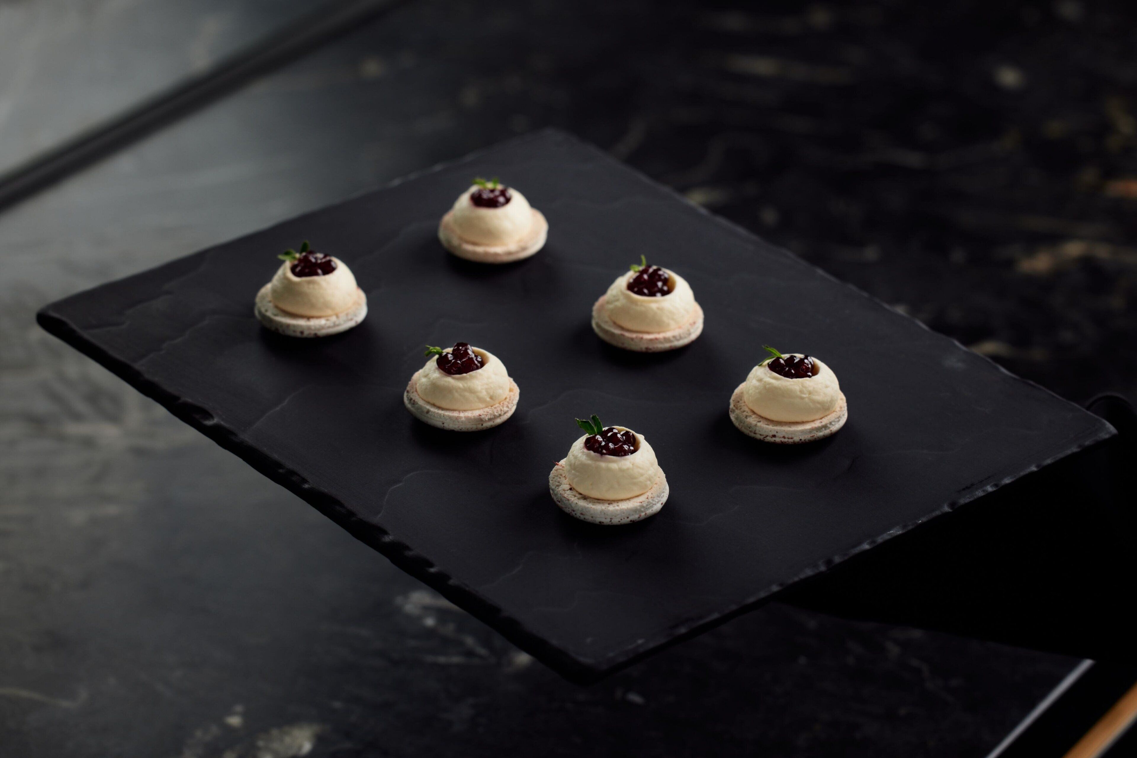 Ett svart skifferbricka med sex små desserter arrangerade i två rader.