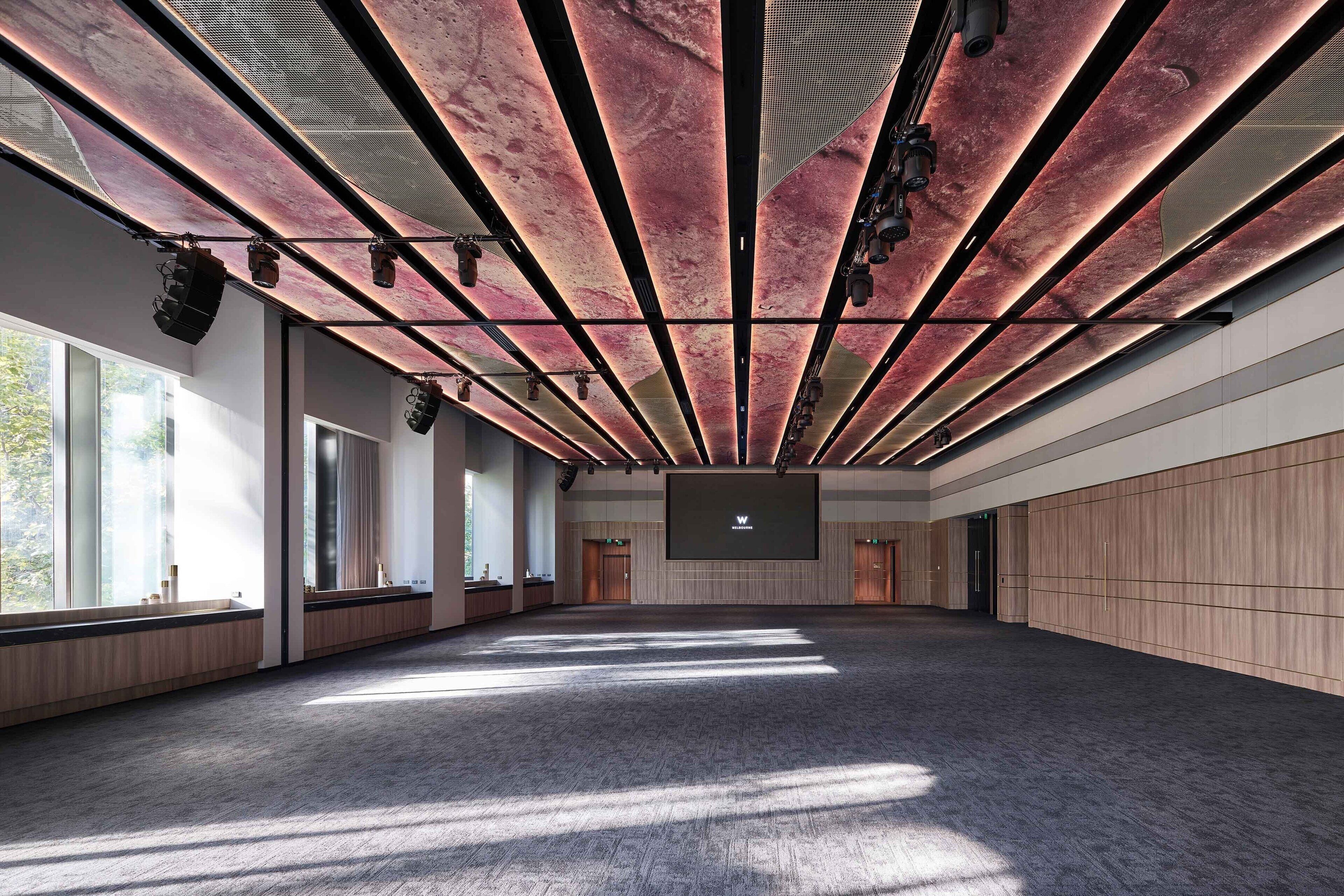 Una amplia sala de conferencias con techo alto, ventanas grandes y una pantalla de proyección central.