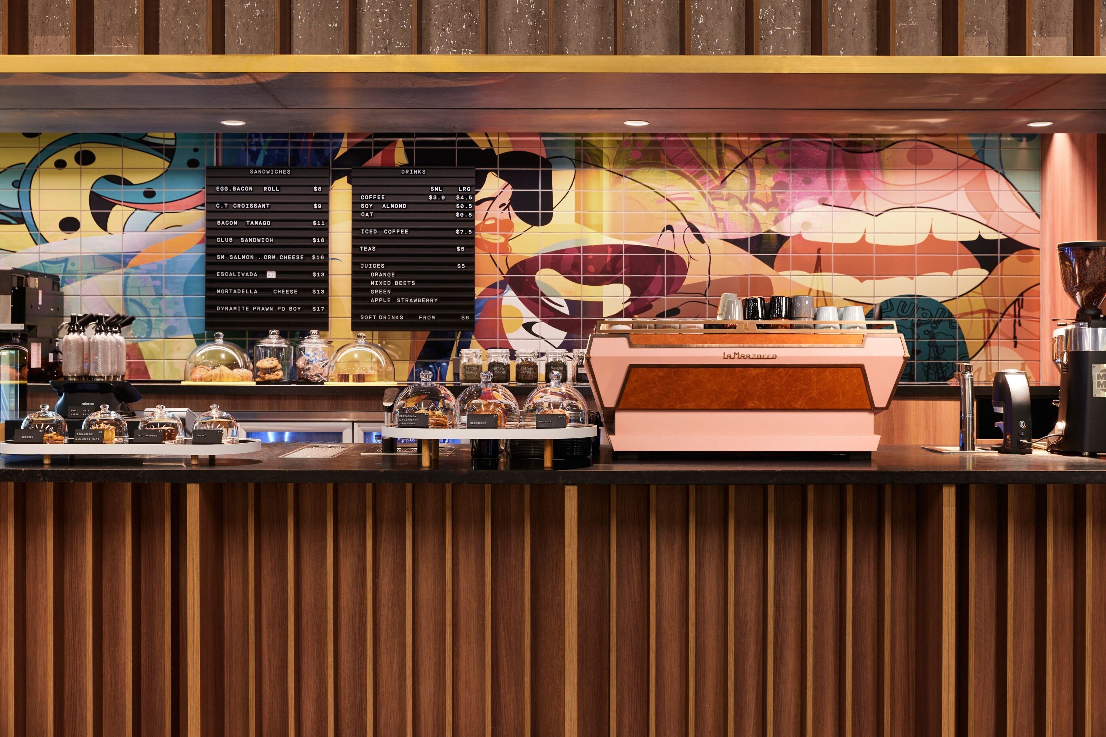 A coffee shop counter with a menu board, coffee machine, and various food items displayed.