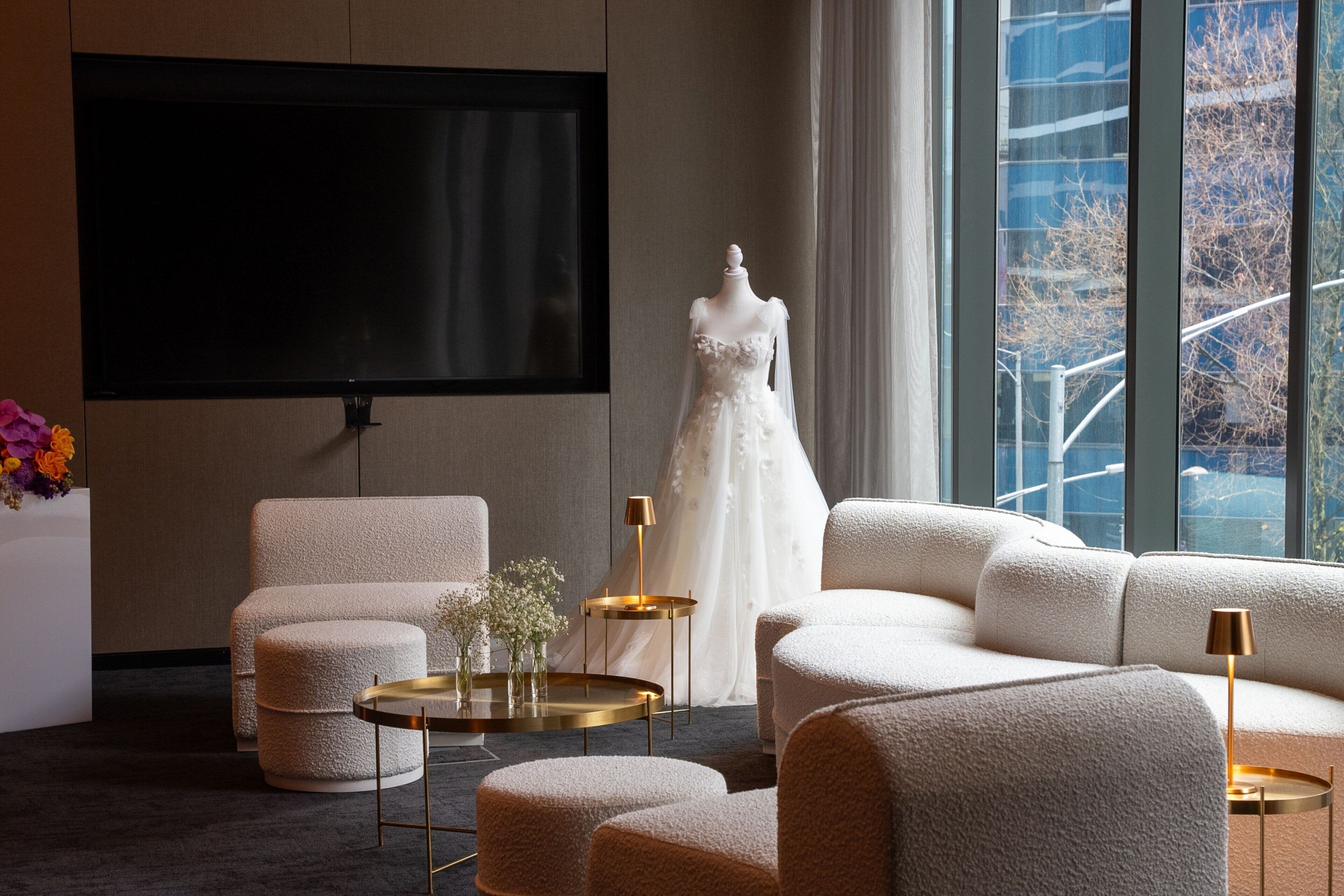 Un salon moderne doté d’un grand téléviseur à écran plat, de fauteuils confortables, d’une robe exposée sur un mannequin et offrant une vue sur l’extérieur.