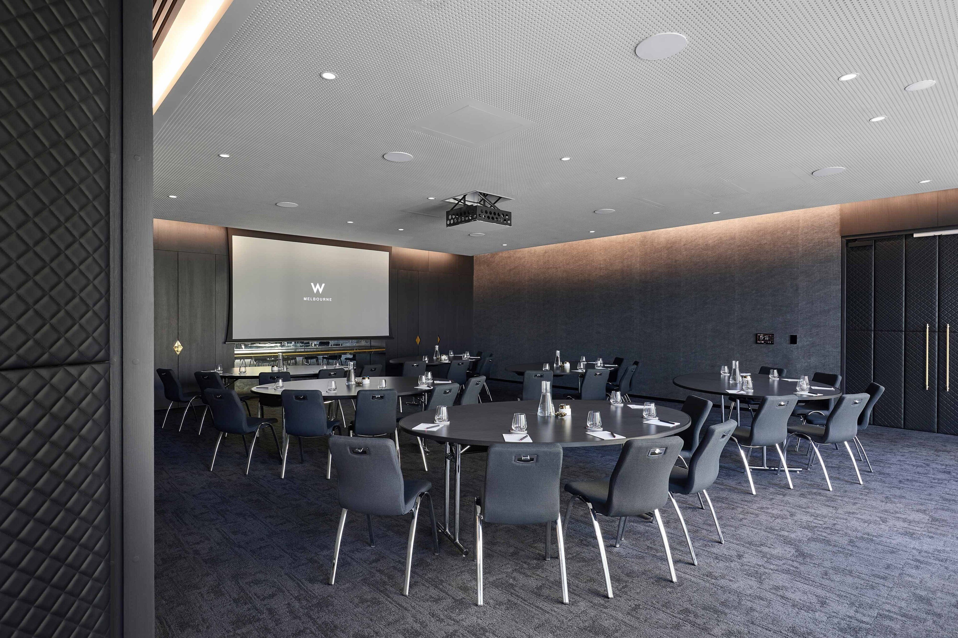 A conference room with round tables, black chairs, and a large screen.