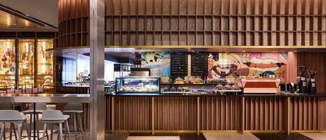 Un área de bar moderna con una barra de madera curva, taburetes y una pantalla con la carta.