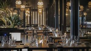 A restaurant with multiple tables set for dining, featuring modern lighting fixtures and a view of the cityscape through large windows. - Amber Kampot (Kampot)