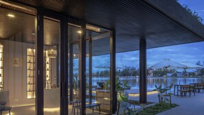 A modern spa with a glass facade, outdoor seating, and a view of a lake. - Amber Kampot (Kampot)