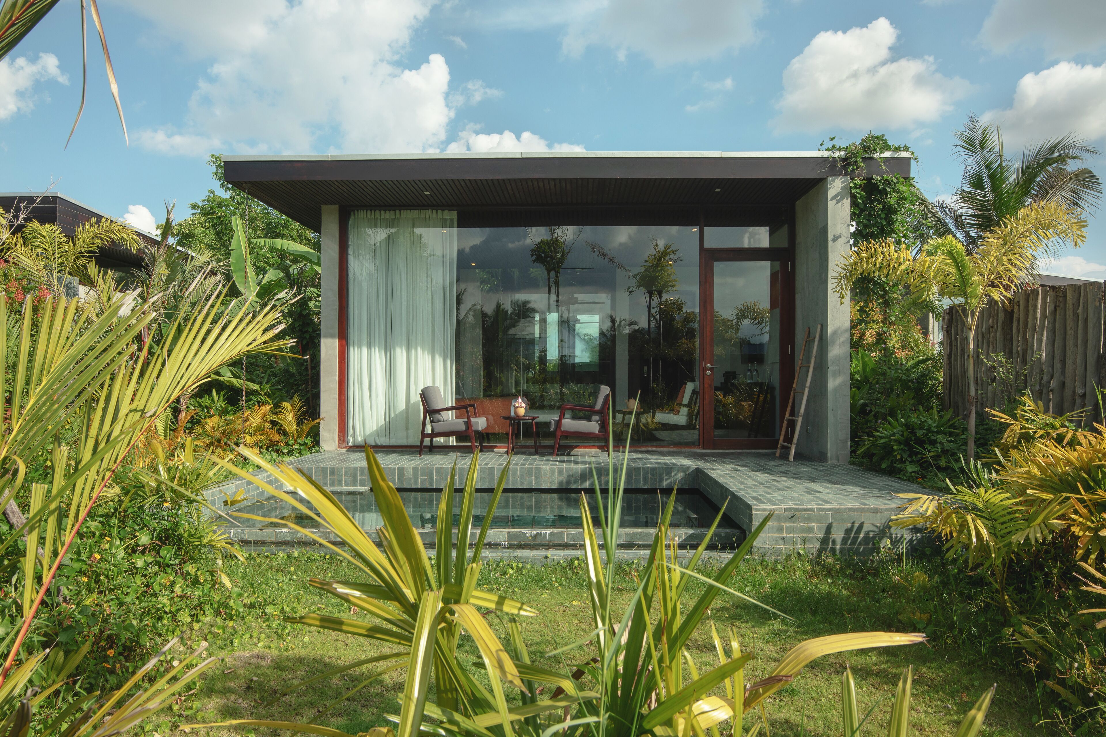 A modern house with a glass door, a patio with chairs, and a swimming pool.