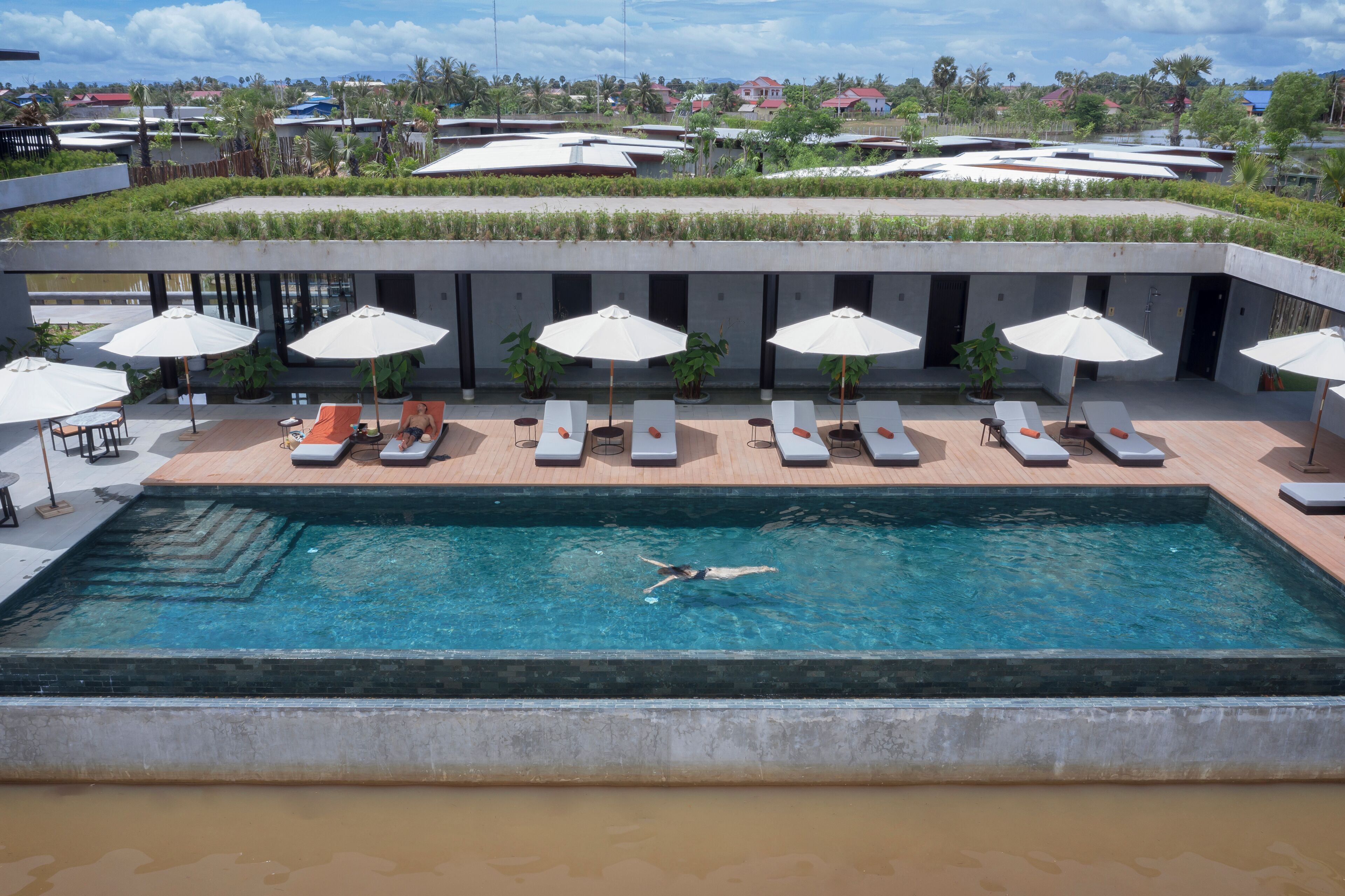 A swimming pool with lounge chairs and umbrellas, surrounded by a modern building with a view of the landscape.