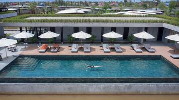 A swimming pool with lounge chairs and umbrellas, surrounded by a modern building with a view of the landscape.