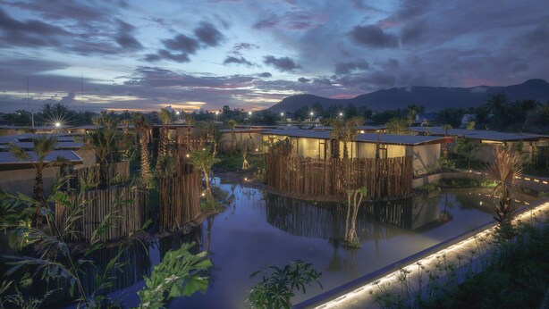 A serene hotel setting with multiple buildings surrounded by water, palm trees, and a mountainous backdrop. - Amber Kampot (Kampot)