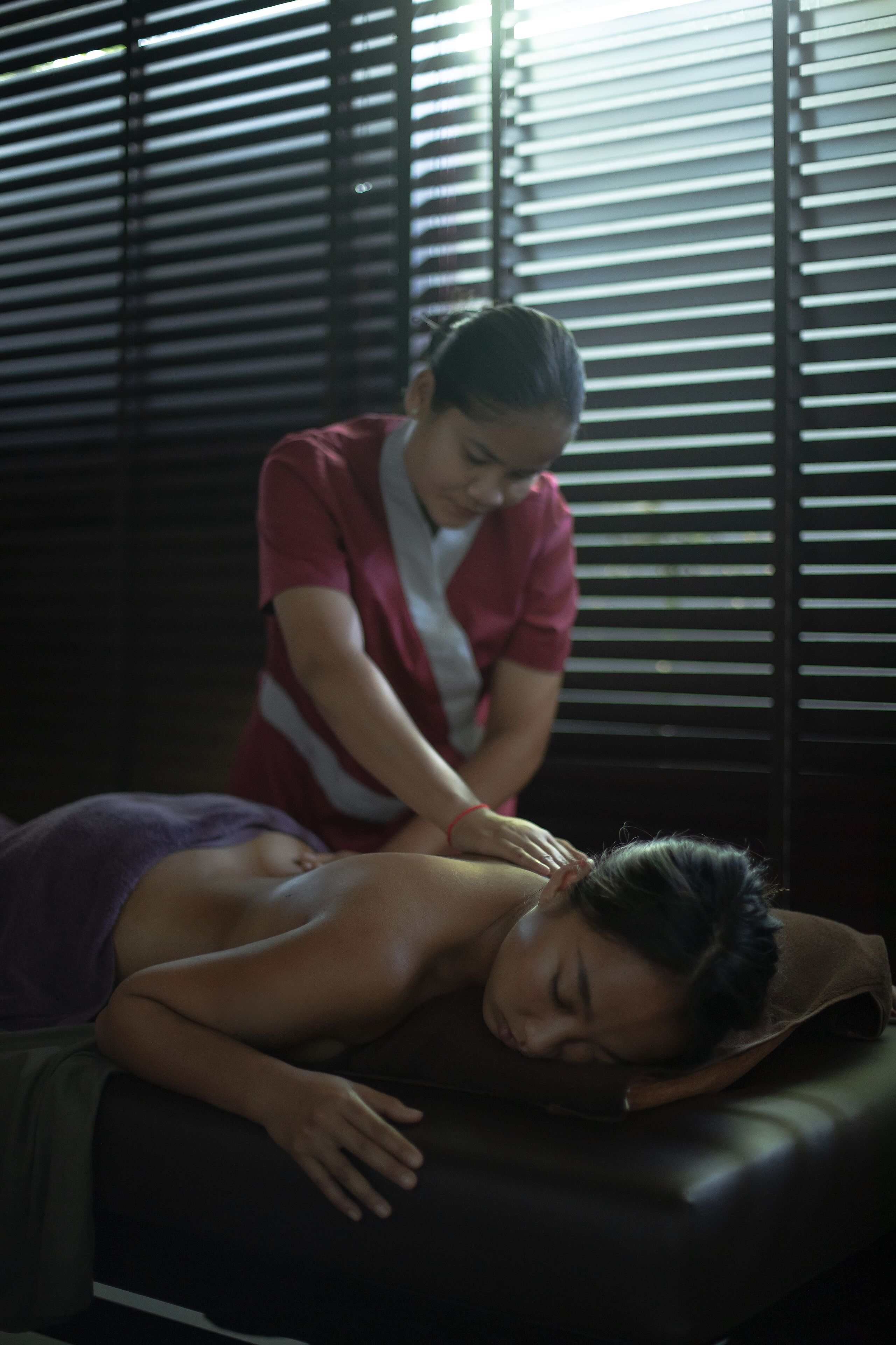 A massage therapy session in a dimly lit room with a massage table and a person receiving a back massage.