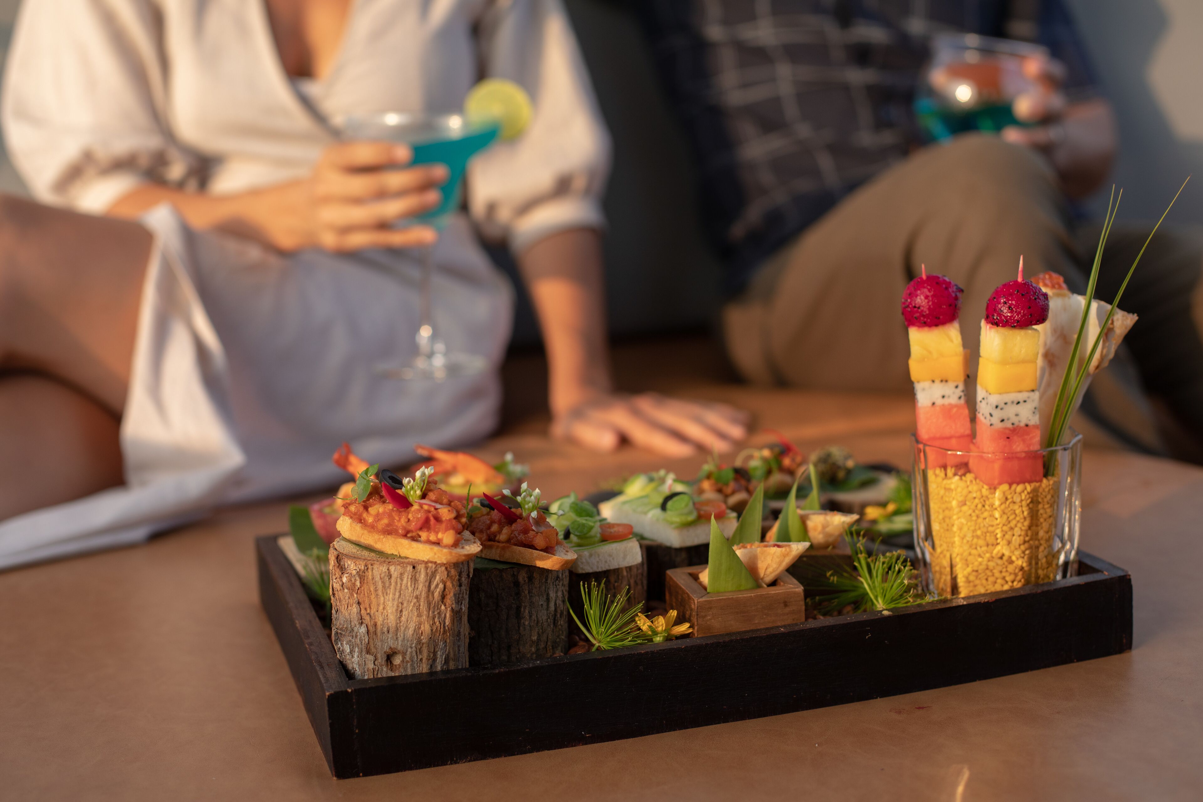 A tray of appetizers on a table with a person in the background holding a drink.