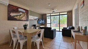 A spacious room with a dining area, a sofa, and a TV. - Riverview Holiday Apartment 60 - Ground Floor -  Kalbarri WA (Kalbarri)