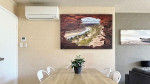 A conference room with a wooden table, white chairs, a potted plant, and a large landscape painting on the wall. - Riverview Holiday Apartment 60 - Ground Floor -  Kalbarri WA (Kalbarri)