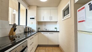 A compact kitchen with white cabinets, a black countertop, a stainless steel stove, and a microwave. - Riverview Holiday Apartment 60 - Ground Floor -  Kalbarri WA (Kalbarri)