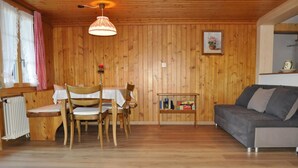 Une pièce aux murs lambrés, comprenant une table à manger, des chaises, un canapé et une petite étagère avec quelques objets.