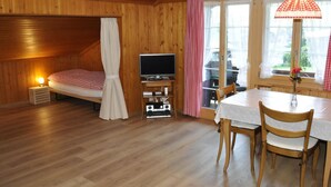 Une pièce confortable avec un lit, une télévision, une table avec des chaises et une fenêtre avec des rideaux.