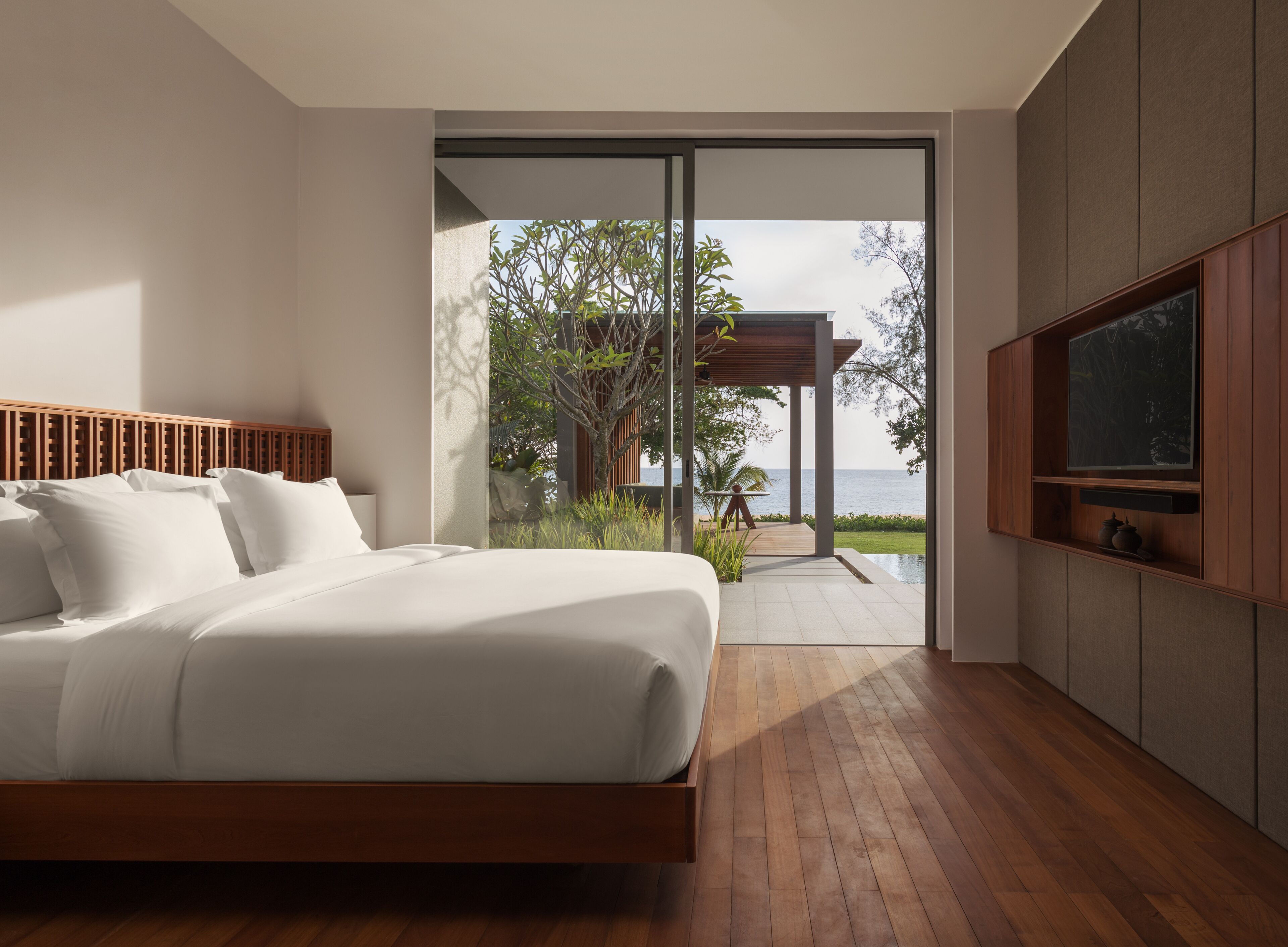 Un dormitorio moderno con una cama grande, un televisor montado en la pared y vistas al mar a través de un ventanal corredero.