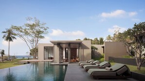 Un espace moderne aménagé au bord de la piscine, avec des chaises longues, une structure entièrement vitrée et une vue sur l’océan.