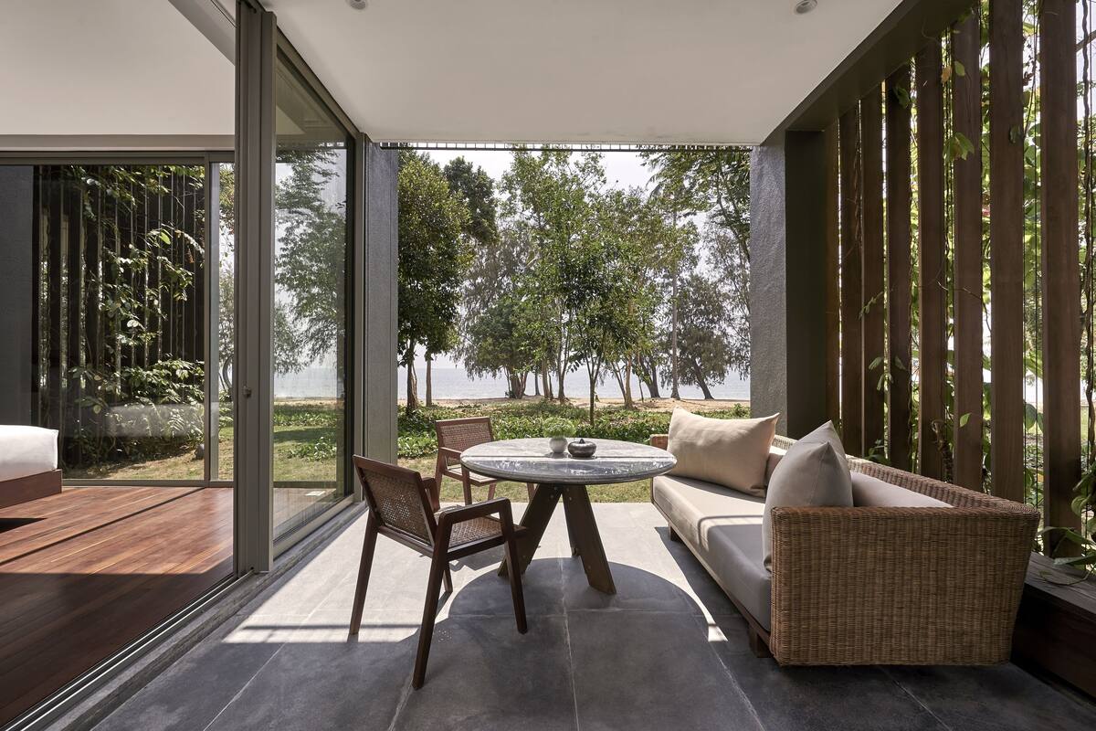 Un espace de détente extérieur moderne, doté d'une table ronde, d'un canapé en osier et offrant une vue sur une plage et des arbres.