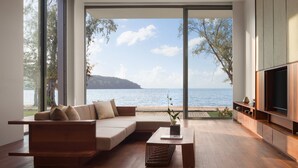 Un salon moderne doté d’une grande fenêtre donnant sur une plage et la mer.