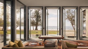 Une chambre moderne dotée de grandes portes vitrées donnant sur la plage, de meubles en osier et d’une table en bois.