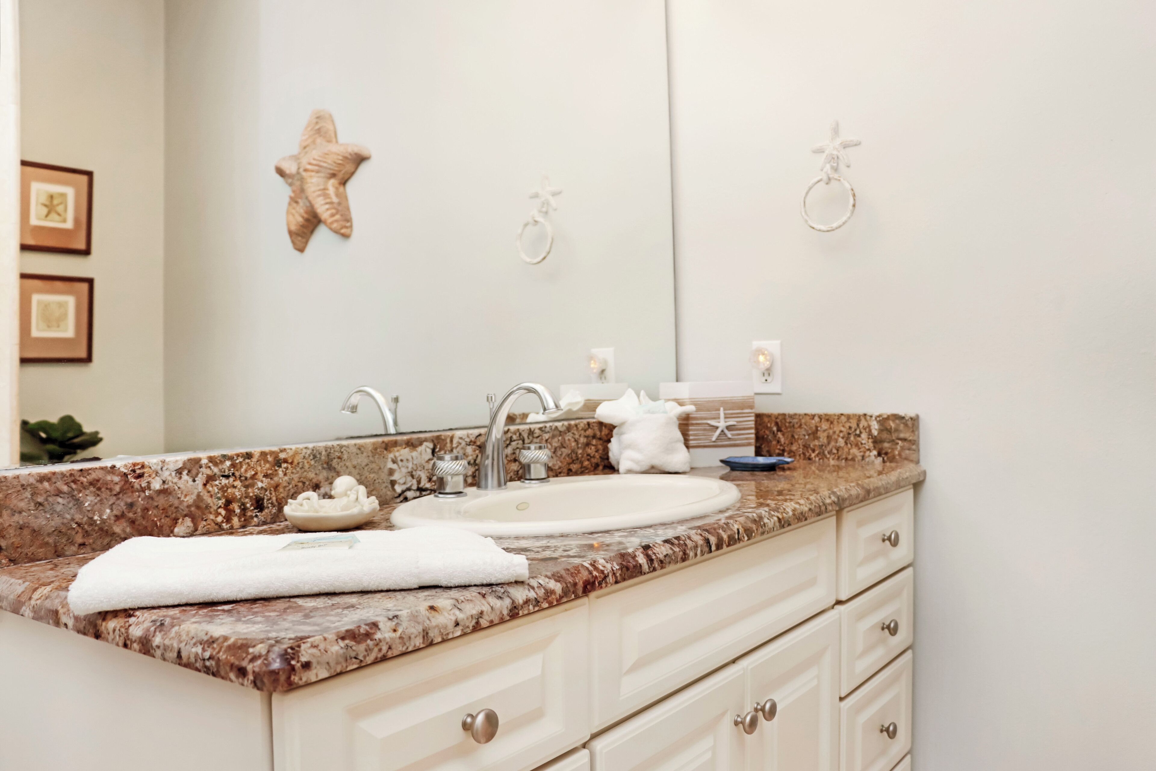Baño con encimera de granito, lavabo, espejo y estrellas de mar decorativas.