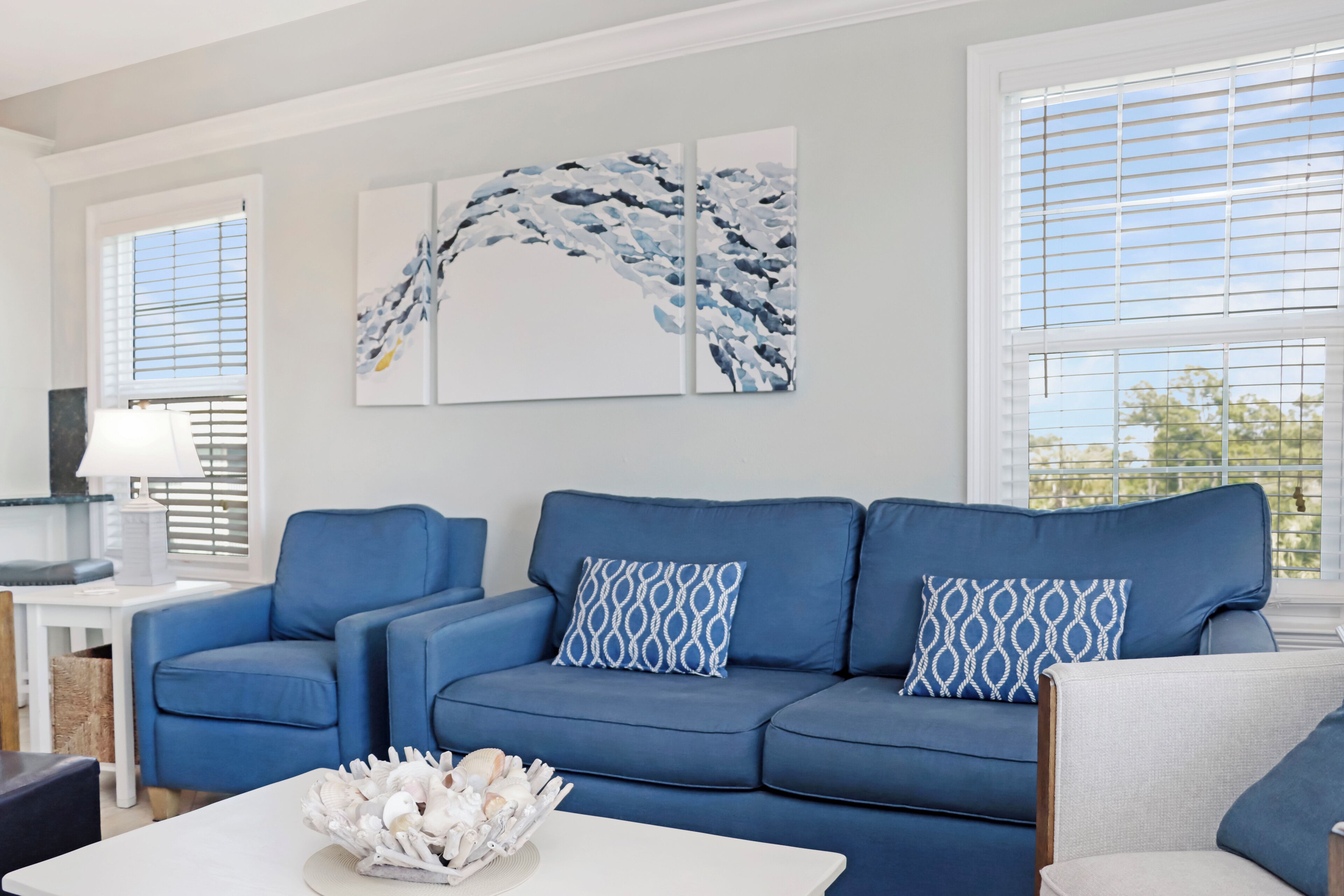 A living room with a blue sofa, patterned pillows, a white coffee table, and abstract wall art.