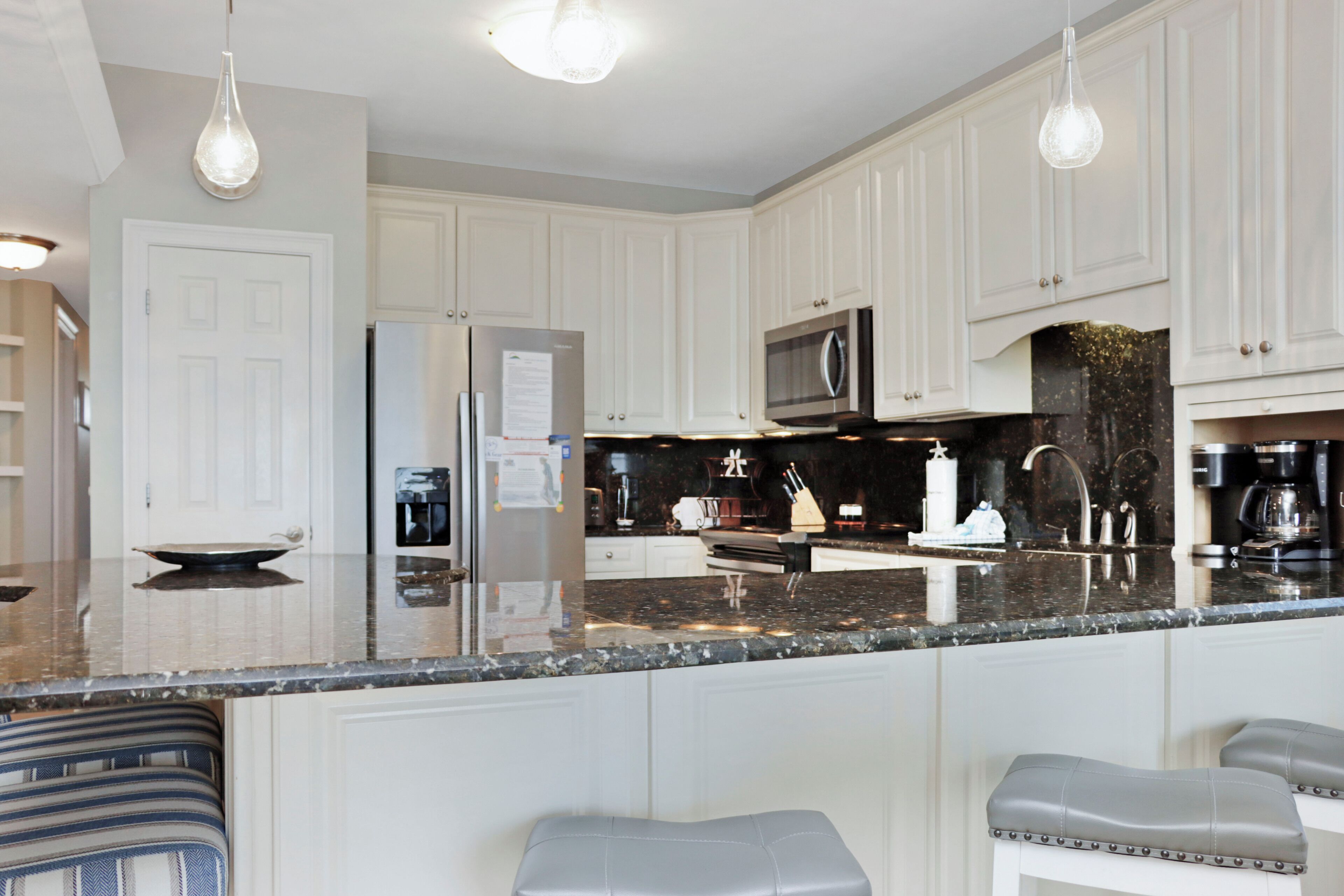 A kitchen with white cabinets, a stainless steel refrigerator, a microwave, and a granite countertop.