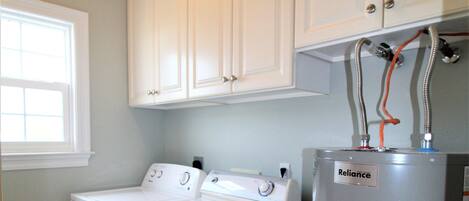 A laundry room with a front-loading washer and dryer, a water heater, and white cabinetry above.