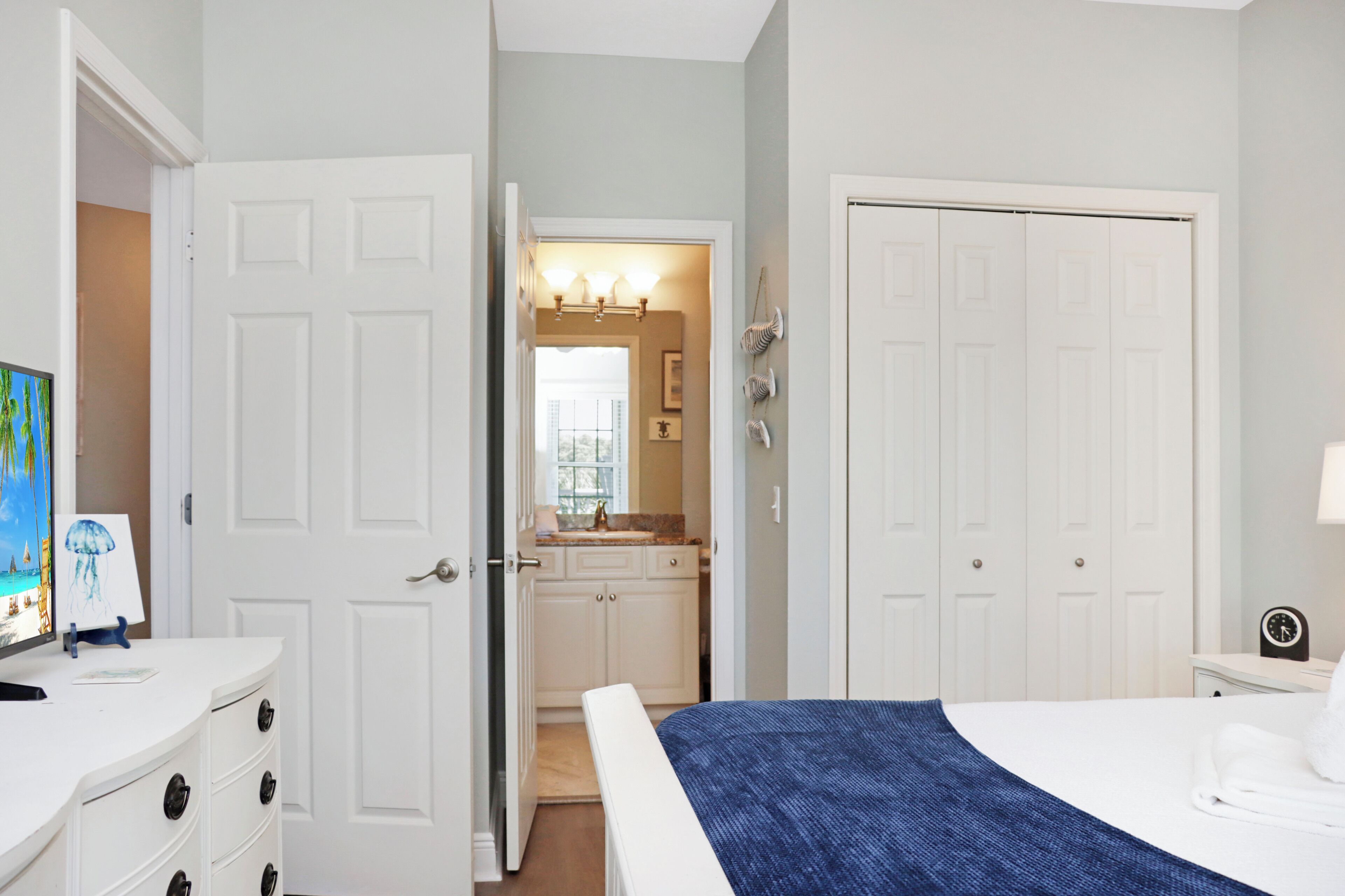 A bedroom with a bed, a dresser, a TV, and a bathroom visible through an open door.