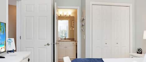 A bedroom with a bed, a dresser, a TV, and a bathroom visible through an open door.
