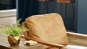 Una cocina moderna con una mesa de comedor de madera y sillas, un sillón de cuero marrón, y una mesita de madera con una planta.