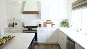 Una cocina moderna con armarios blancos, estufa a gas, lavavajillas y encimera de madera.