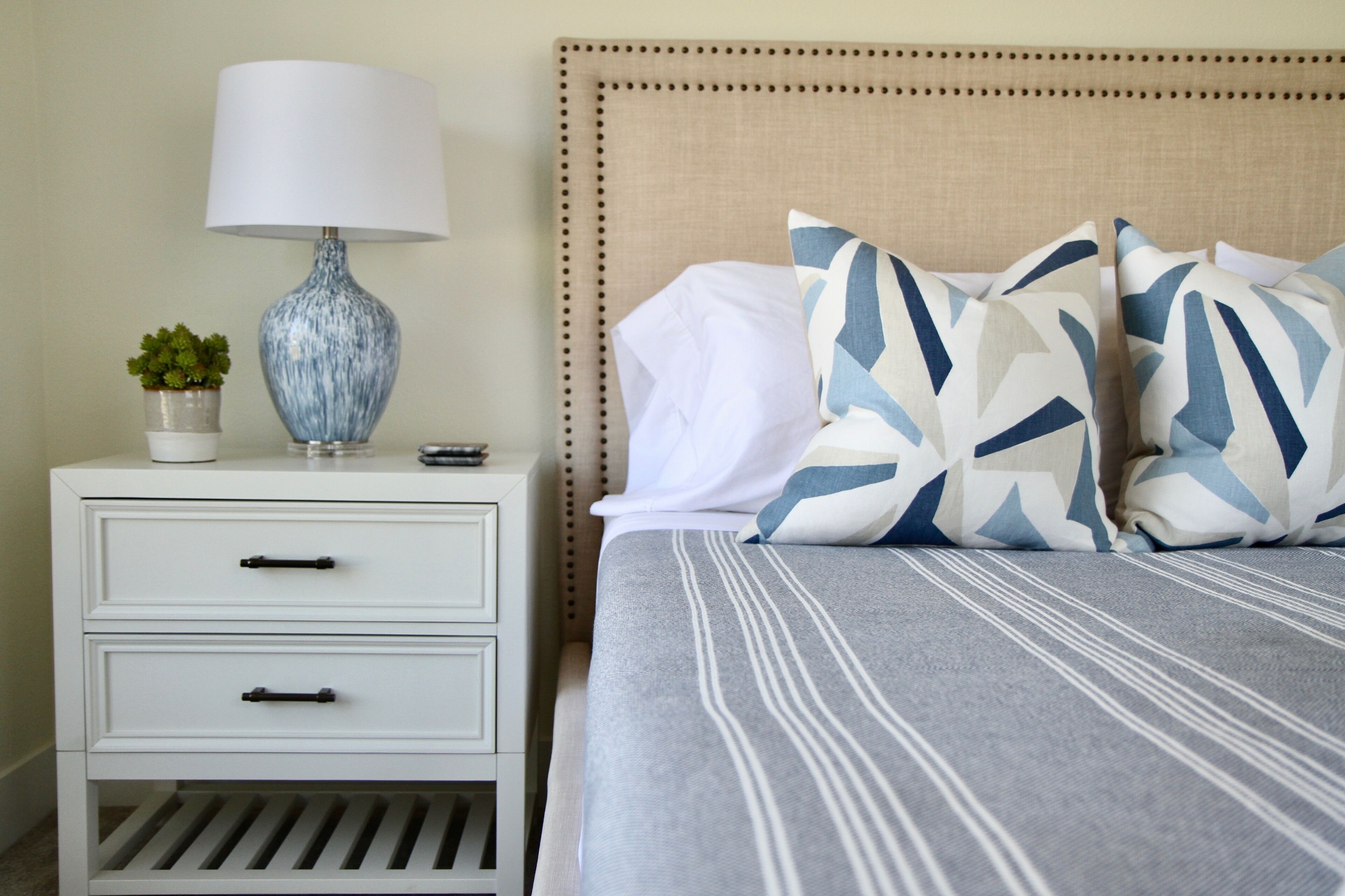 A neatly made bed with striped bedding, a bedside lamp, and decorative pillows.