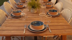 Un área de comedor al aire libre con una mesa de madera preparada para seis personas, rodeada de sillas de mimbre.