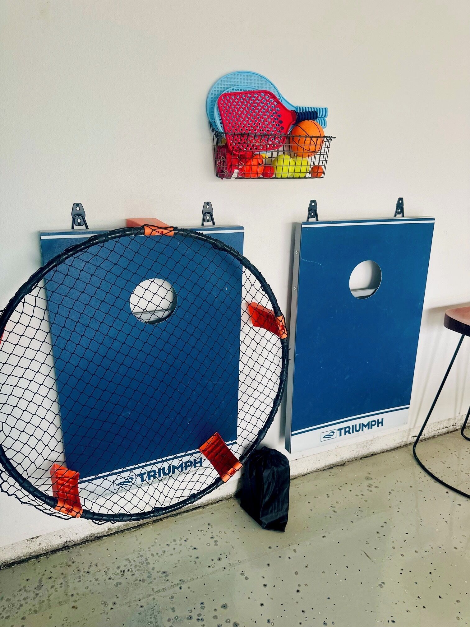 A tennis court with a net, blue storage units, and a basket with sports equipment.