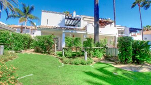 A white building with a tiled roof, surrounded by a well-maintained garden with palm trees and shrubs. - 1176 Beachfront Paradise in Bahia de Marbella (Marbella)