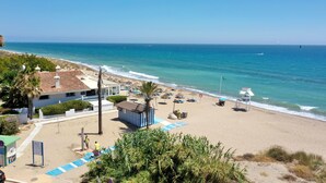 A beach with a clear view of the ocean, a few umbrellas, and a small building. - 1176 Beachfront Paradise in Bahia de Marbella (Marbella)