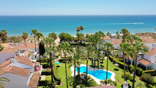 A resort with a swimming pool surrounded by palm trees and a view of the ocean. - 1176 Beachfront Paradise in Bahia de Marbella (Marbella)
