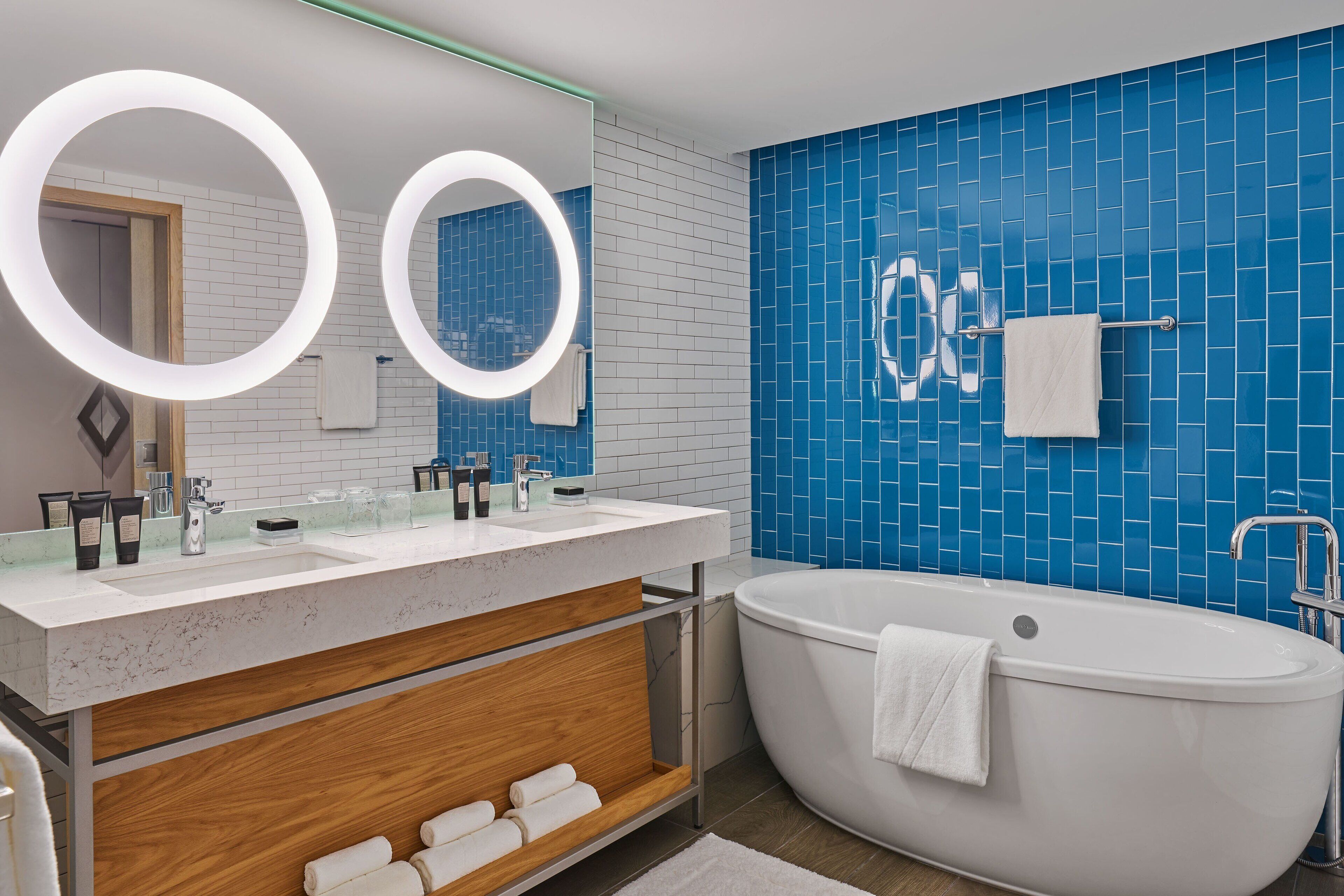 A modern bathroom with a freestanding bathtub, a vanity with a mirror, and blue-tiled walls.