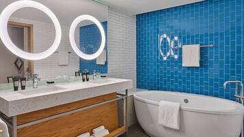 A modern bathroom with a freestanding bathtub, a vanity with a mirror, and blue-tiled walls.