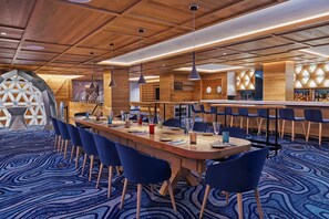 Un moderno vestíbulo de hotel con un largo mostrador de recepción de madera, sillas azules y una alfombra estampada.