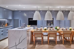 Una cocina moderna con isla de mármol, mesa de comedor de madera e iluminación colgante.
