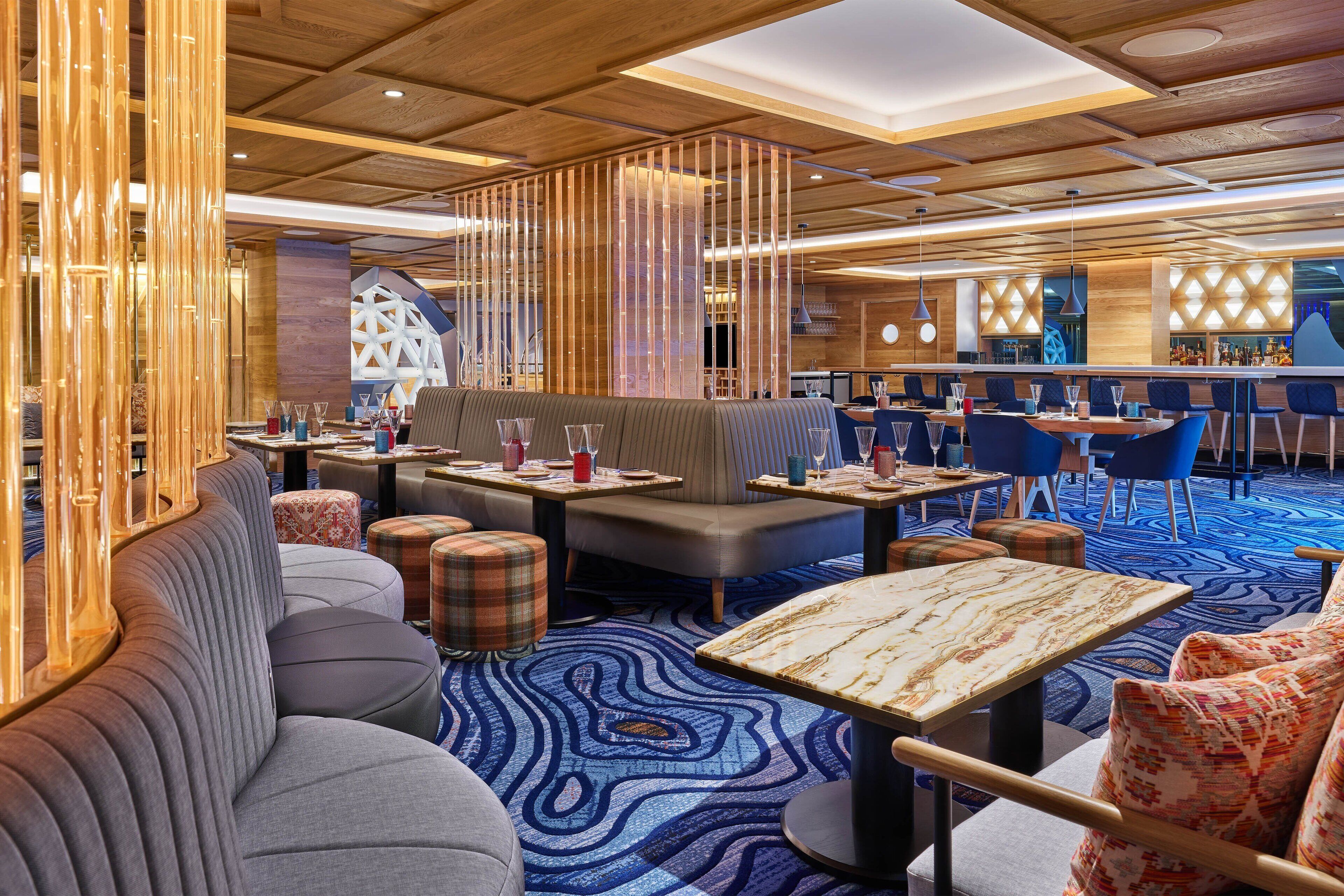 Un hall d’hôtel moderne, doté d’espaces aménagés avec des sièges, d’un bar et d’un tapis à motifs.